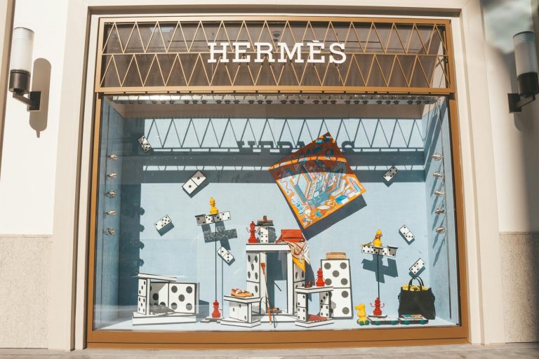 Artistic window display at a Hermes store featuring domino-themed decor and luxury items.